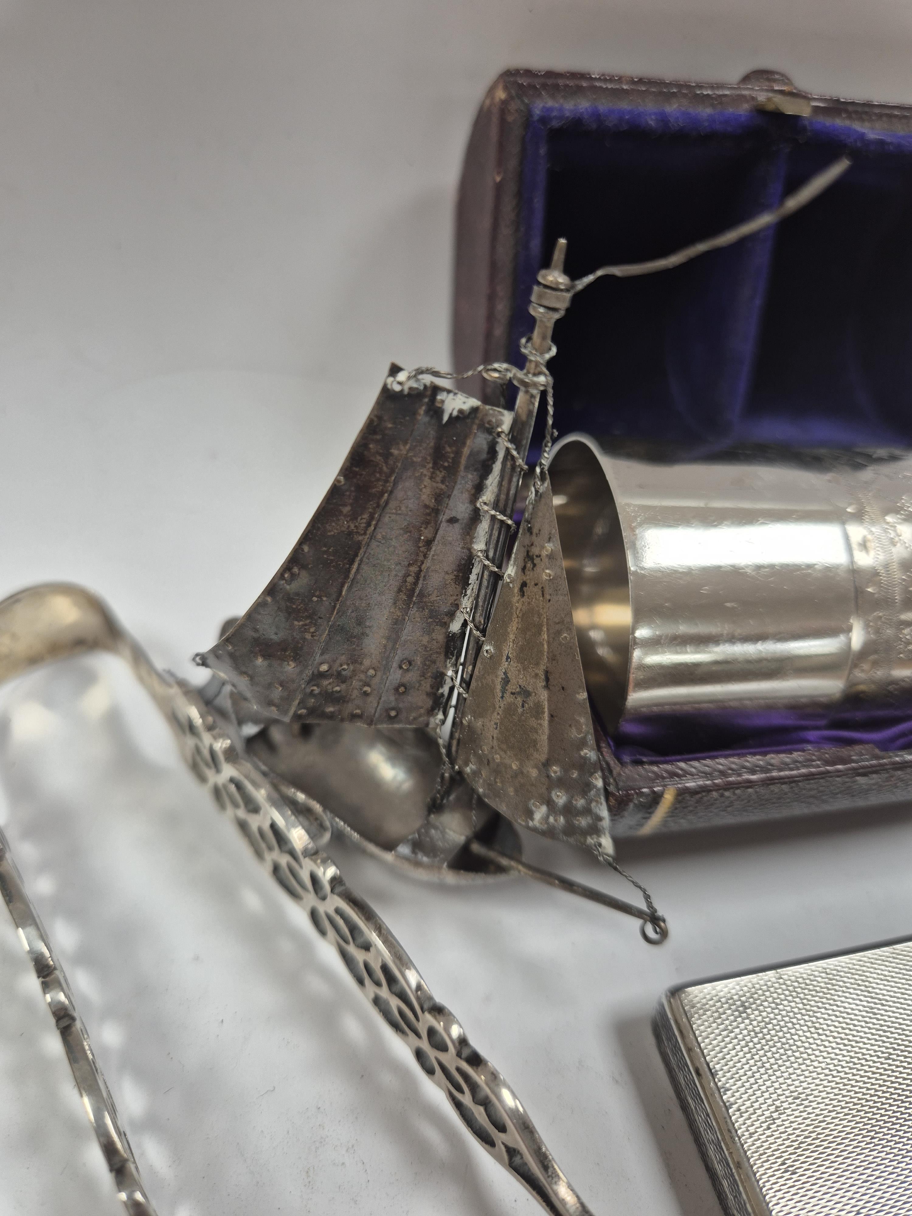 A 1930's engine turned silver cigarette case, 88mm, two silver napkin rings, a white metal miniature model of a boat and a pair of Georgian silver sugar tongs (a.f.). Condition - poor to fair